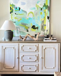 a white dresser with a large painting on it